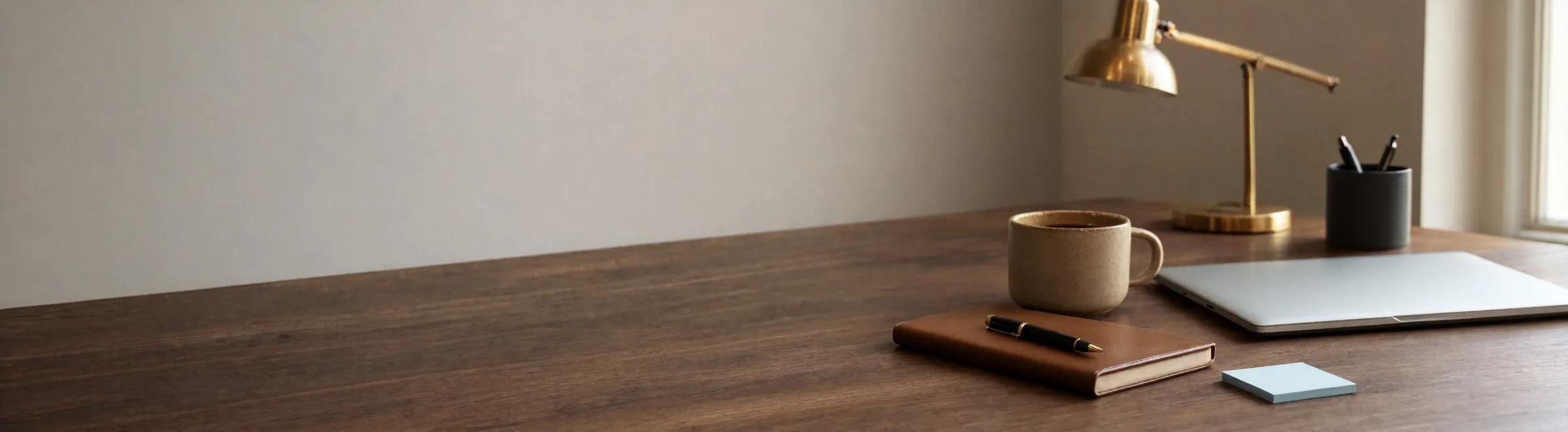 Banner Donation Benefits A Walnut Desk By A Window With A Brass Task Lamp, A Ceramic Mug Of Coffee, A Leather Notebook With A Fountain Pen Resting On It, And A Closed Laptop