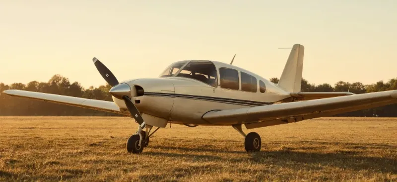 A Small Single-Engine Propeller Plane Parked On A Grass Airstrip In Low Golden Light